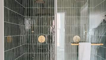 Un baño moderno con ducha envuelta en vidrio, paredes de azulejos verde oscuro y piso cubierto de azulejos blancos.