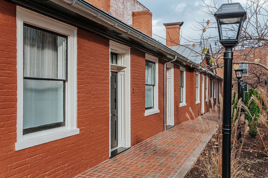 A row of red brick townhouses with white-framed windows and doors, a brick pathway, and a black street lamp.