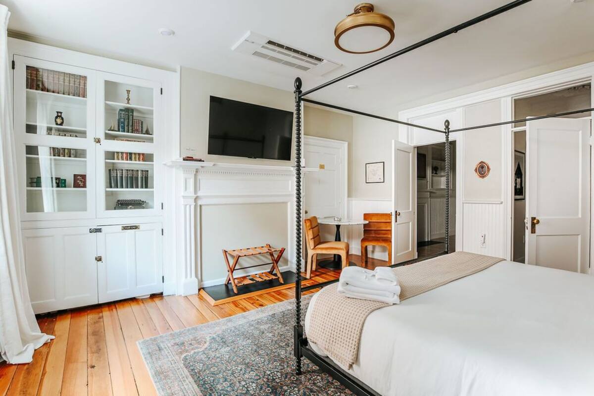 A bedroom with a four-poster bed, a fireplace, a bookshelf, and a television.