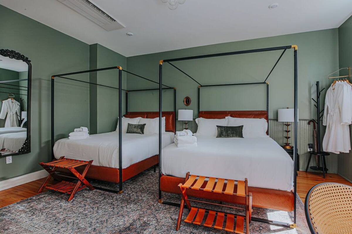 A hotel room with two four-poster beds, a small wooden bench, a chair, and a mirror.