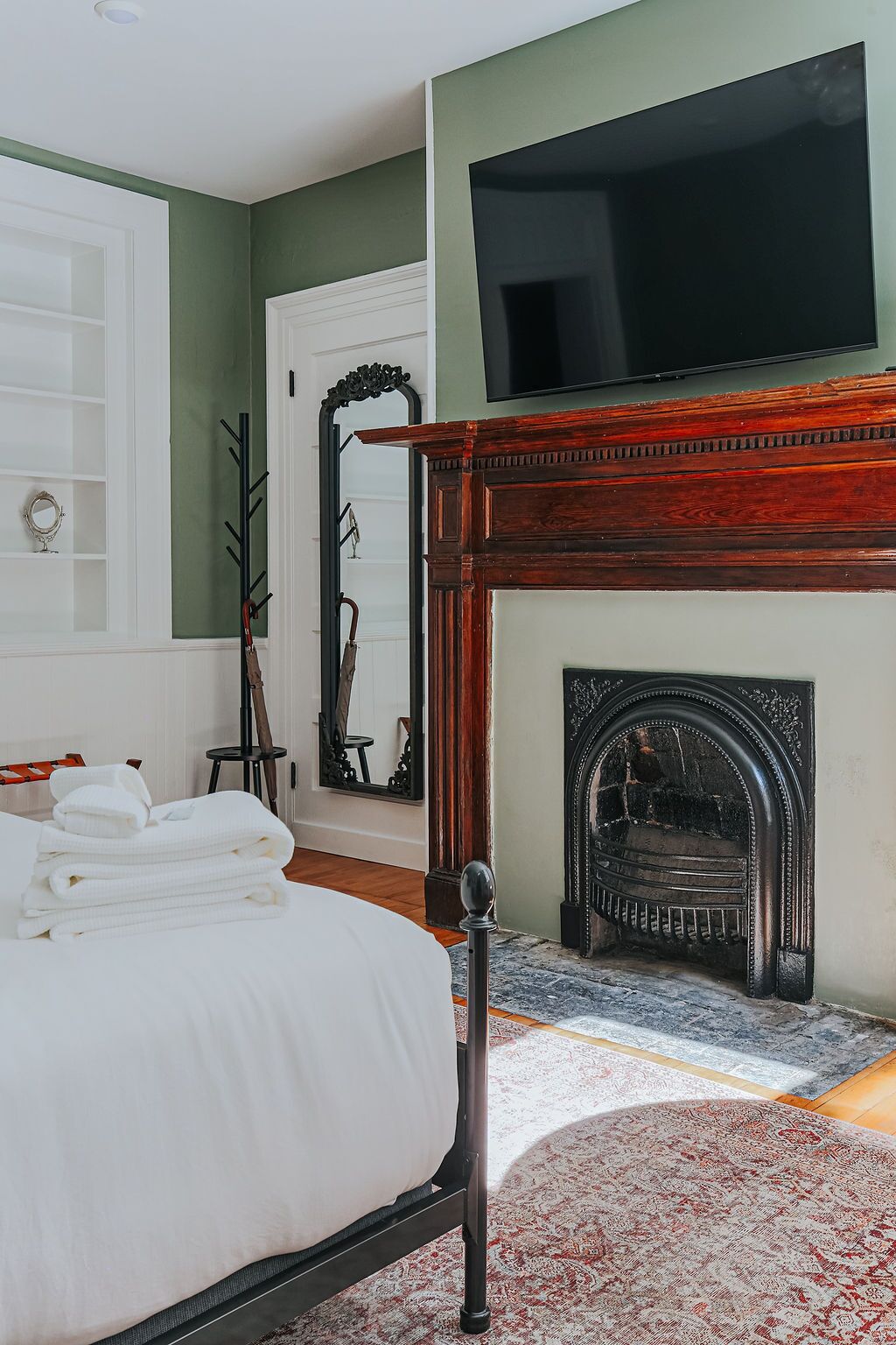 A bedroom with a bed, a fireplace, a TV, and a coat rack.