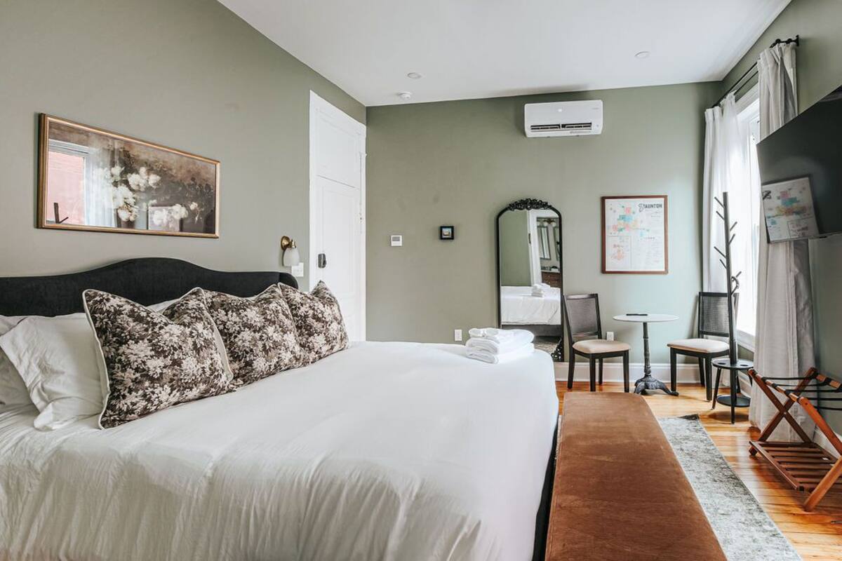 A neatly arranged bedroom with a large bed, a bedside table, a mirror, and a small desk with chairs.