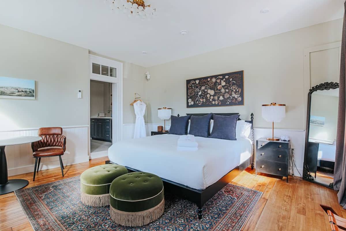 A bedroom with a large bed, two ottomans, a desk, and a chair.