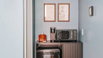 Une cuisine compacte équipée d’une cuisinière intégrée, d’un four à micro-ondes et d’une machine à café. Deux tableaux encadrés ornent le mur, ainsi qu’un petit meuble et un plancher en bois.