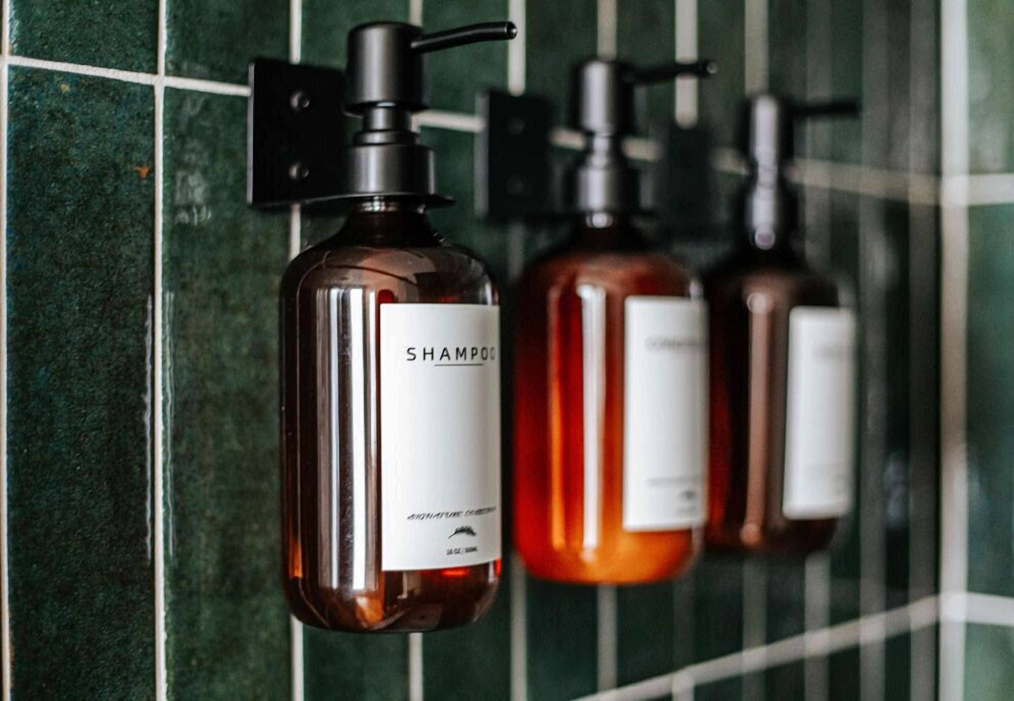 Tre flaconi di shampoo appesi a una parete piastrellata.