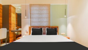 A modern hotel room with a large bed, wooden headboard, bedside tables, and a desk with a chair. - Abssolute Homtel - Rooms and Suites  (Pune)