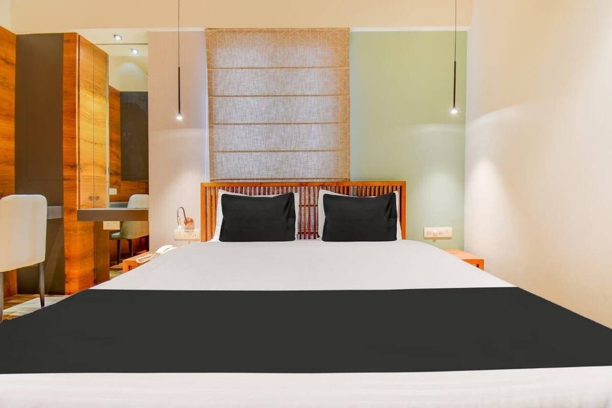 A modern hotel room with a large bed, wooden headboard, bedside tables, and a desk with a chair.
