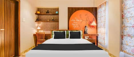 A hotel room with a large bed, a wooden headboard, a nightstand, a lamp, a shelf with decorative items, and a wall with a floral pattern.