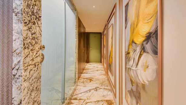 A hallway with marble flooring, framed artwork on the walls, and a door at the end. - Abssolute Homtel - Rooms and Suites  (Pune)