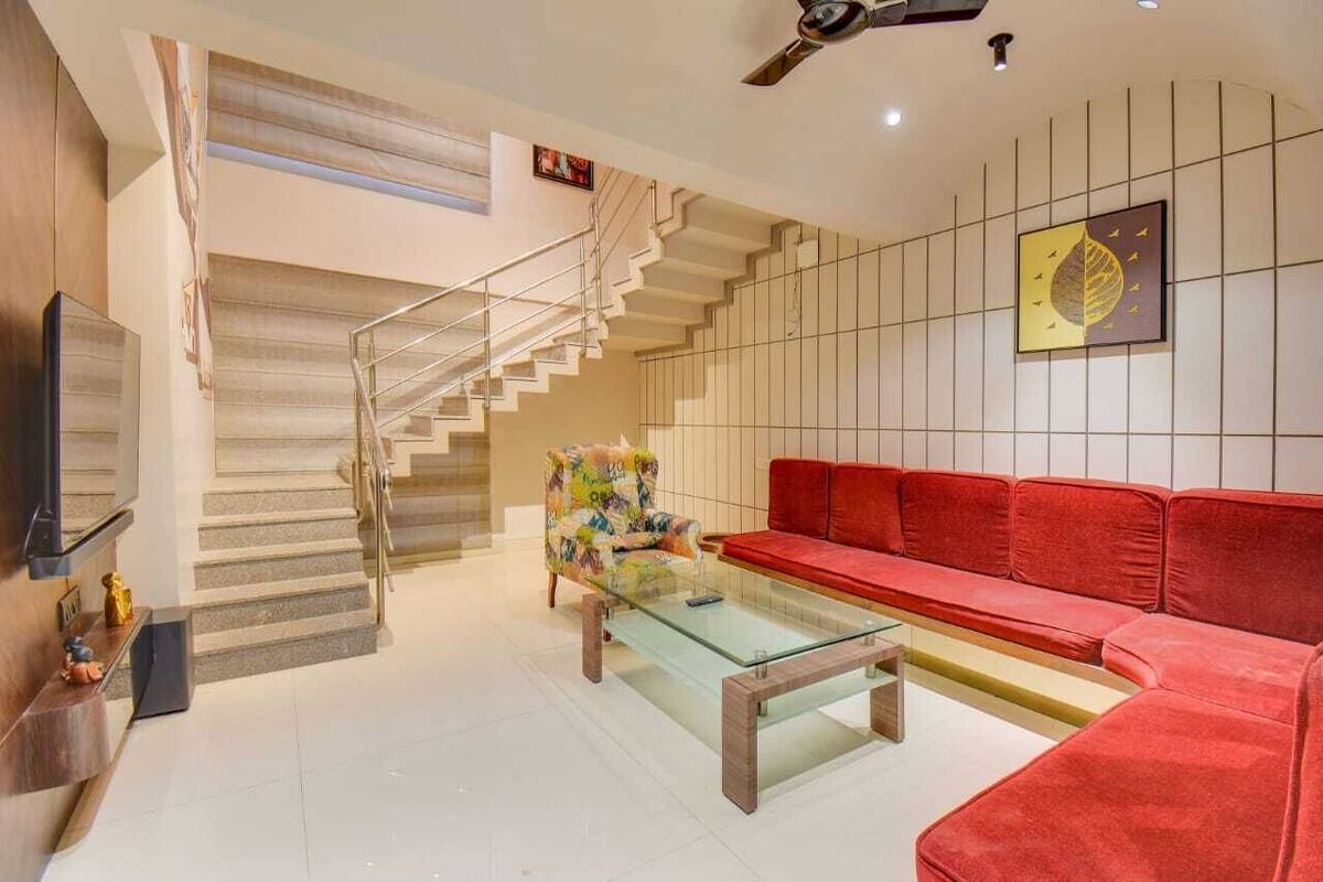 A modern living room with a staircase, a red sofa, a glass coffee table, and a colorful armchair.
