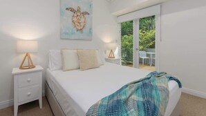 Une chambre à coucher comprenant un lit, une table de chevet, une lampe, un tableau et une porte-fenêtre coulissante donnant sur un balcon.