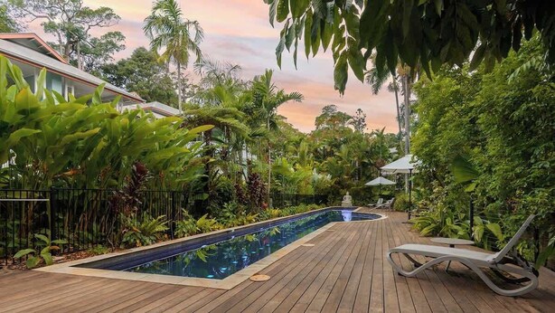 Une terrasse en bois avec une piscine, entourée d’une végétation luxuriante et agrémentée d’un belvédère.