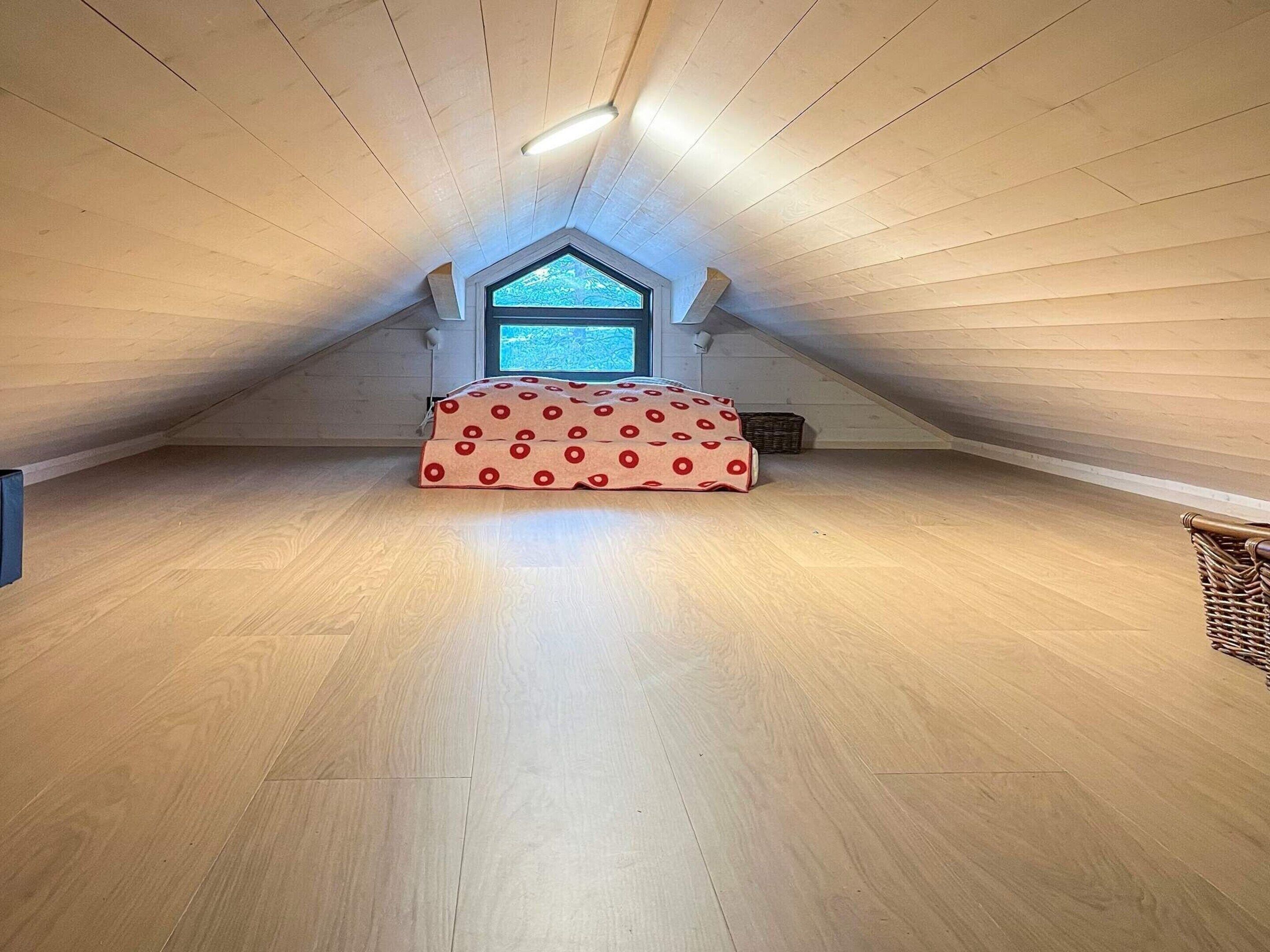 Ampia camera da letto mansardata con soffitto spiovente, una grande finestra e un letto con copriletto a pois rossi.