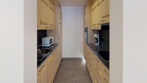 A narrow kitchen with wooden cabinets and a black countertop. - Luxury Apartment With View (Veysonnaz)