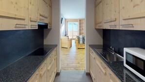 A narrow kitchen with wooden cabinets and black countertops. - Luxury Apartment With View (Veysonnaz)