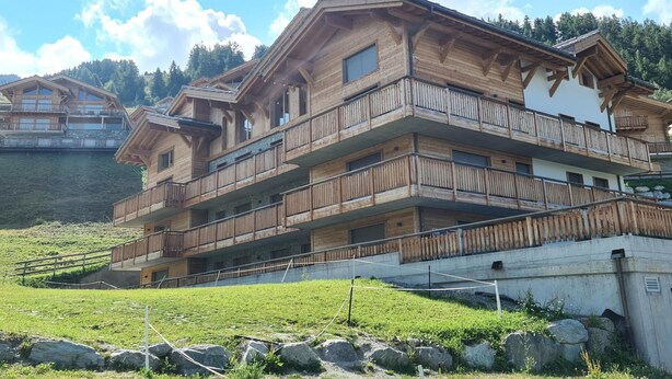A multi-story wooden chalet with balconies, set against a mountainous backdrop. - Luxury Apartment With View (Veysonnaz)