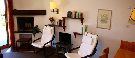 A living room with two white armchairs, a wooden coffee table, a television, a bookshelf, and a fireplace.