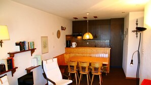 Un salon avec un canapé rouge, une table à manger en bois entourée de chaises, un téléviseur et des étagères à livres.