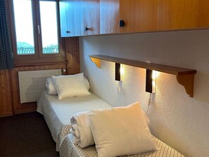 A small, cozy bedroom with a single bed, a wooden headboard, and a window with a view. - Apartment With Nendaz View (Nendaz)
