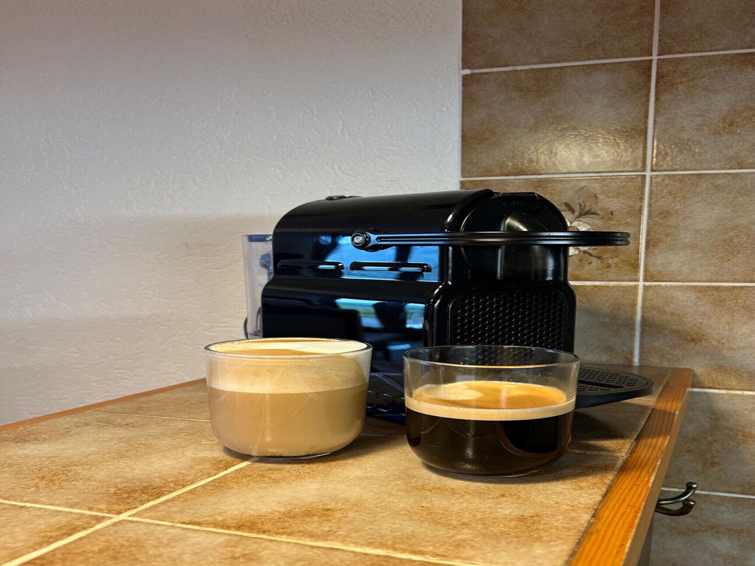 Una cafetera sobre una encimera de cocina con dos tazas de café.