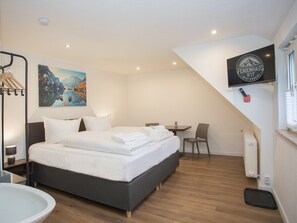 Una habitación de hotel moderna con una cama grande, un escritorio, una silla, un televisor y un cuadro de un paisaje montañoso.