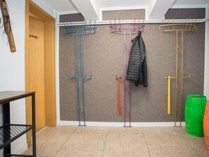 Una habitación con una puerta de madera, un estante de metal negro y cuatro percheros azules, rosas, amarillos y verdes fijados a la pared.