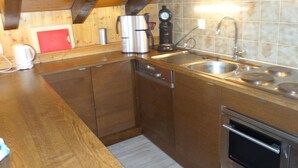 A kitchen with wooden cabinets, a stainless steel sink, a coffee maker, and a clock on the wall. - Apartment With Breathtaking Hill View (Veysonnaz)