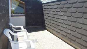 A small outdoor area with a window and a wall covered in shingles. There are two white plastic chairs. - Apartment With Breathtaking Hill View (Veysonnaz)