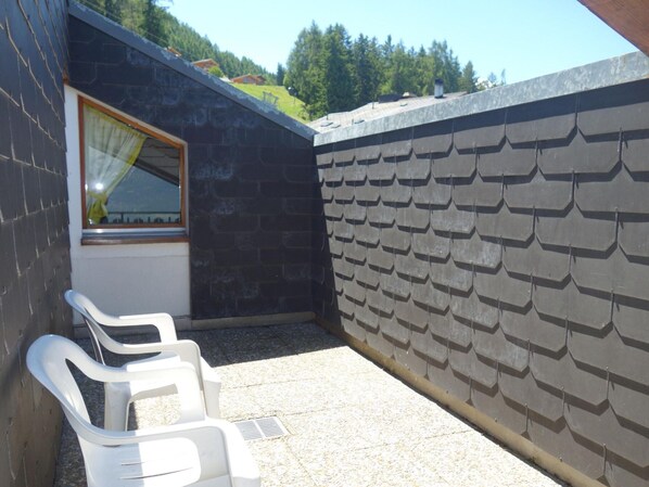 A small outdoor area with a window and a wall covered in shingles. There are two white plastic chairs. - Apartment With Breathtaking Hill View (Veysonnaz)