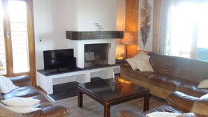 A living room with a fireplace, leather sofas, a coffee table, and a television. - Apartment With Breathtaking Hill View (Veysonnaz)