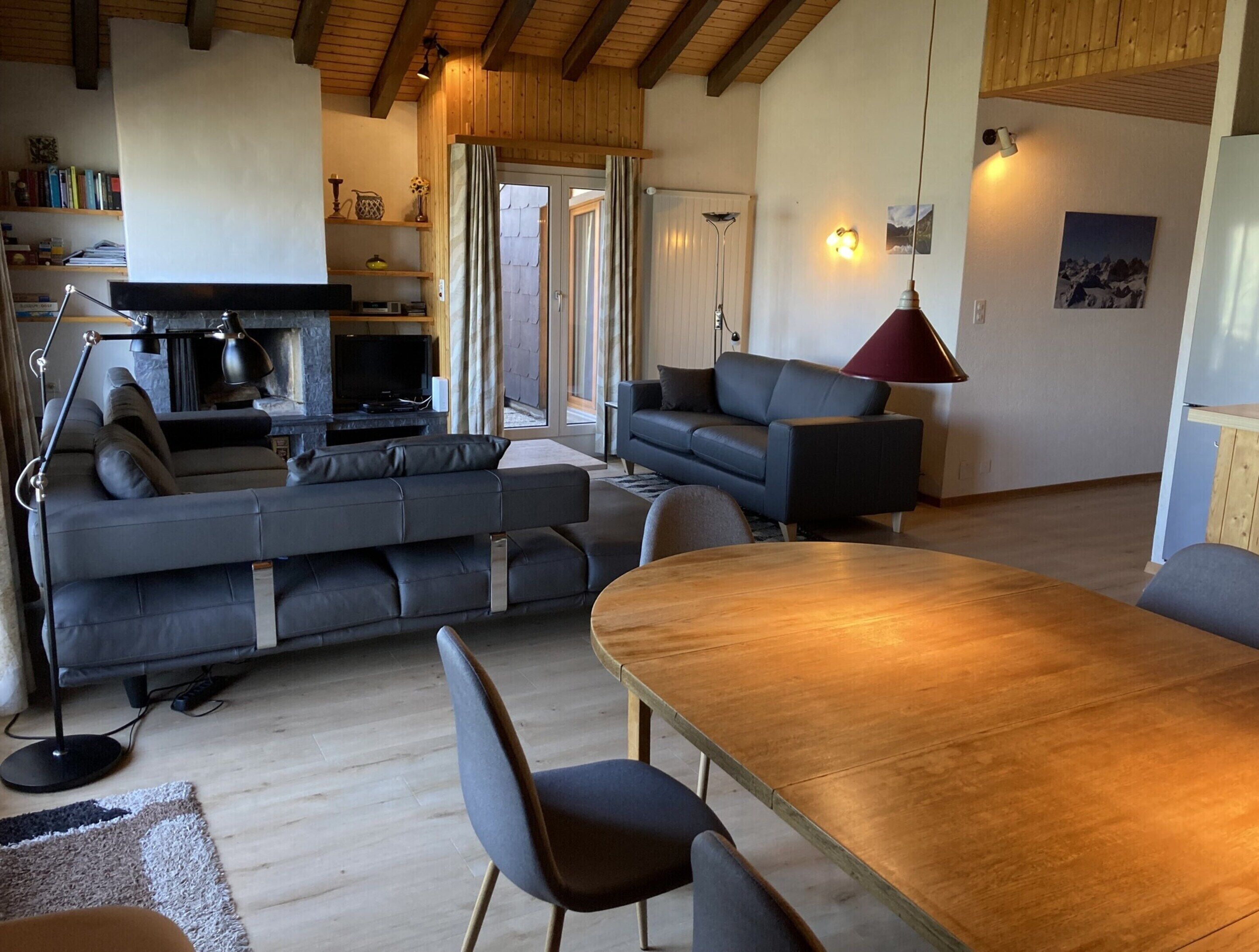 A modern living room with a large sofa, a dining table, and a kitchen area visible through an open door.
