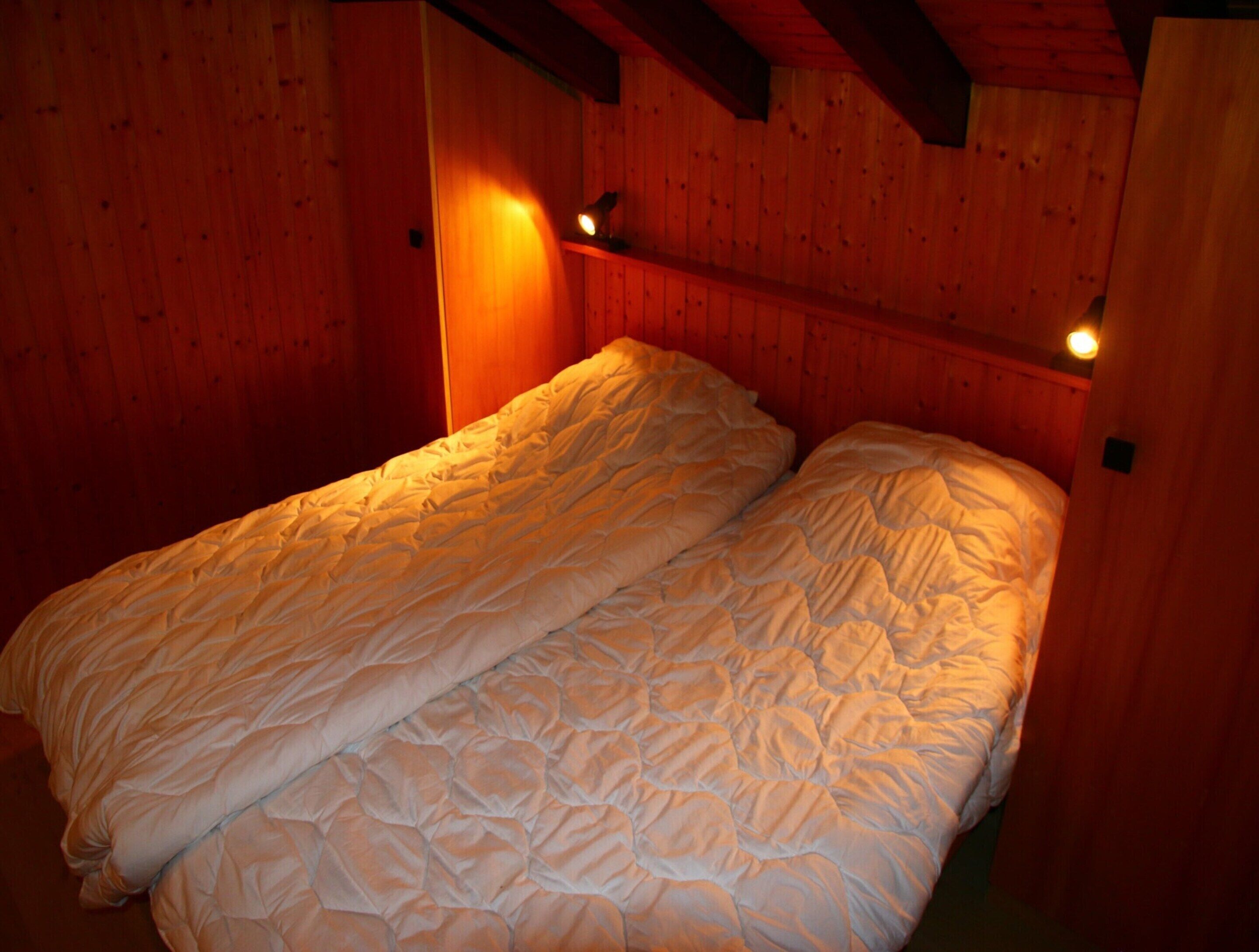 Une pièce aux murs en bois et un lit recouvert d’une couverture matelassée.