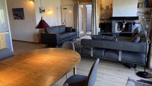 A modern living room with a wooden dining table, grey sofas, and a television. - Peaceful Apartment With Amenities (Veysonnaz)