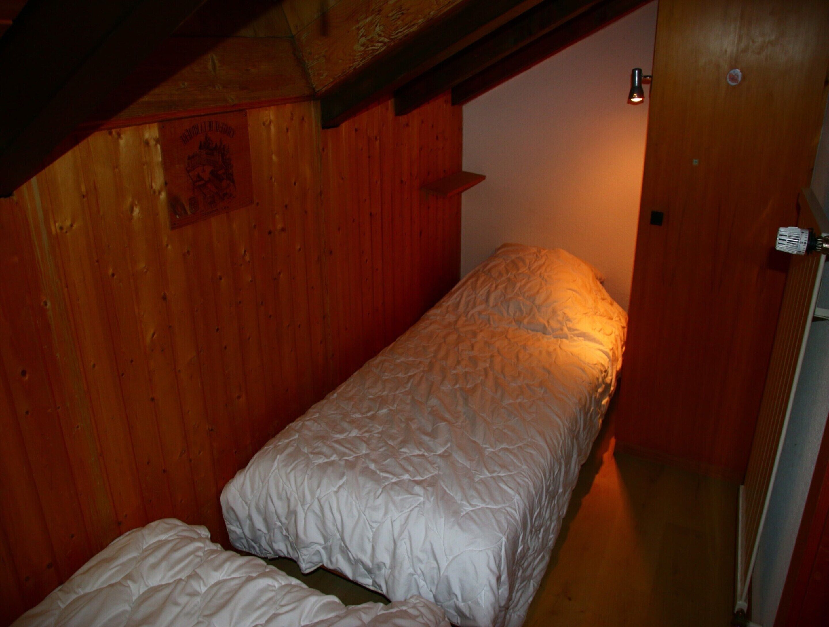 A small, single-bed room with wooden walls and a sloped ceiling.