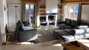 A spacious living room with a fireplace, leather sofas, and a large window offering a view. - Peaceful Apartment With Amenities (Veysonnaz)
