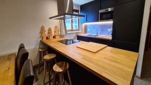 A modern kitchen with a wooden island, bar stools, a stainless steel range hood, and black cabinetry. - Peaceful Apartment With Amenities (Veysonnaz)
