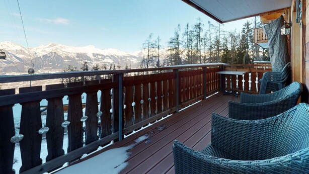 A wooden deck with wicker chairs, a table, and a view of snow-capped mountains. - Cozy Apartment With Sauna (Veysonnaz)