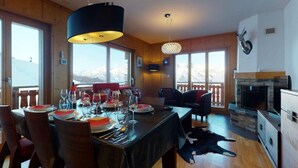 A dining area with a table set for four, a fireplace, and a view of mountains. - Cozy Apartment With Sauna (Veysonnaz)