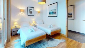 A modern bedroom with two beds, wooden flooring, a large rug, and wall-mounted lamps. - Cozy Apartment With Sauna (Veysonnaz)