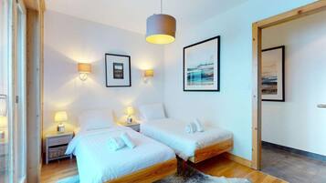 A modern bedroom with two beds, wooden flooring, a large rug, and wall-mounted lamps.