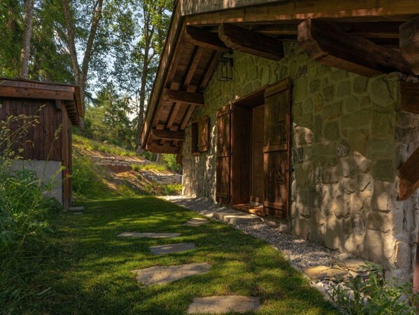 Un bâtiment rustique en pierre, doté d’une porte en bois et d’une petite fenêtre, entouré d’un chemin en pierre et de verdure.