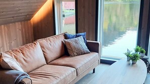 Ein modernes Wohnzimmer mit einer braunen Ledersofa, einem runden Couchtisch und Blick auf ein Gewässer durch große Fenster.