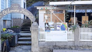 Ein Café namens 'Cafe Odemoris Hage' mit Holzbauweise, Stufen, die zu ihm führen, und einer Schautafel.
