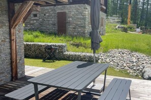 An outdoor patio with a table and benches, stone walls, and a grassy area with a stone wall and a wooden fence. - Luxe Apartment Near ski Lift (Anniviers)