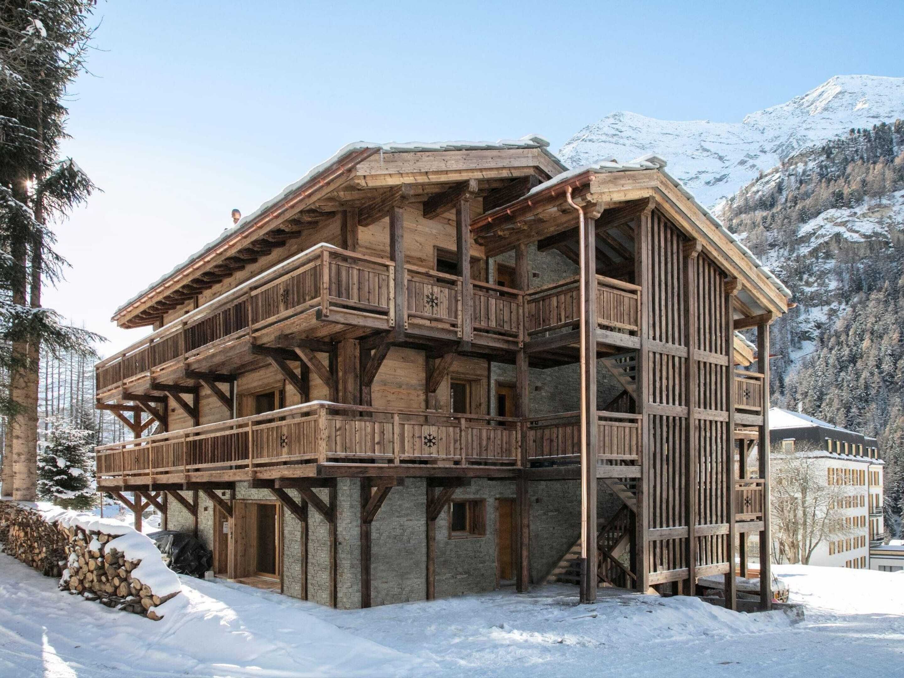 A multi-story wooden chalet with balconies, set in a snowy mountainous area.