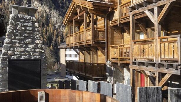 A wooden chalet with a stone fireplace, a hot tub, and wooden balconies overlooking a mountainous area.