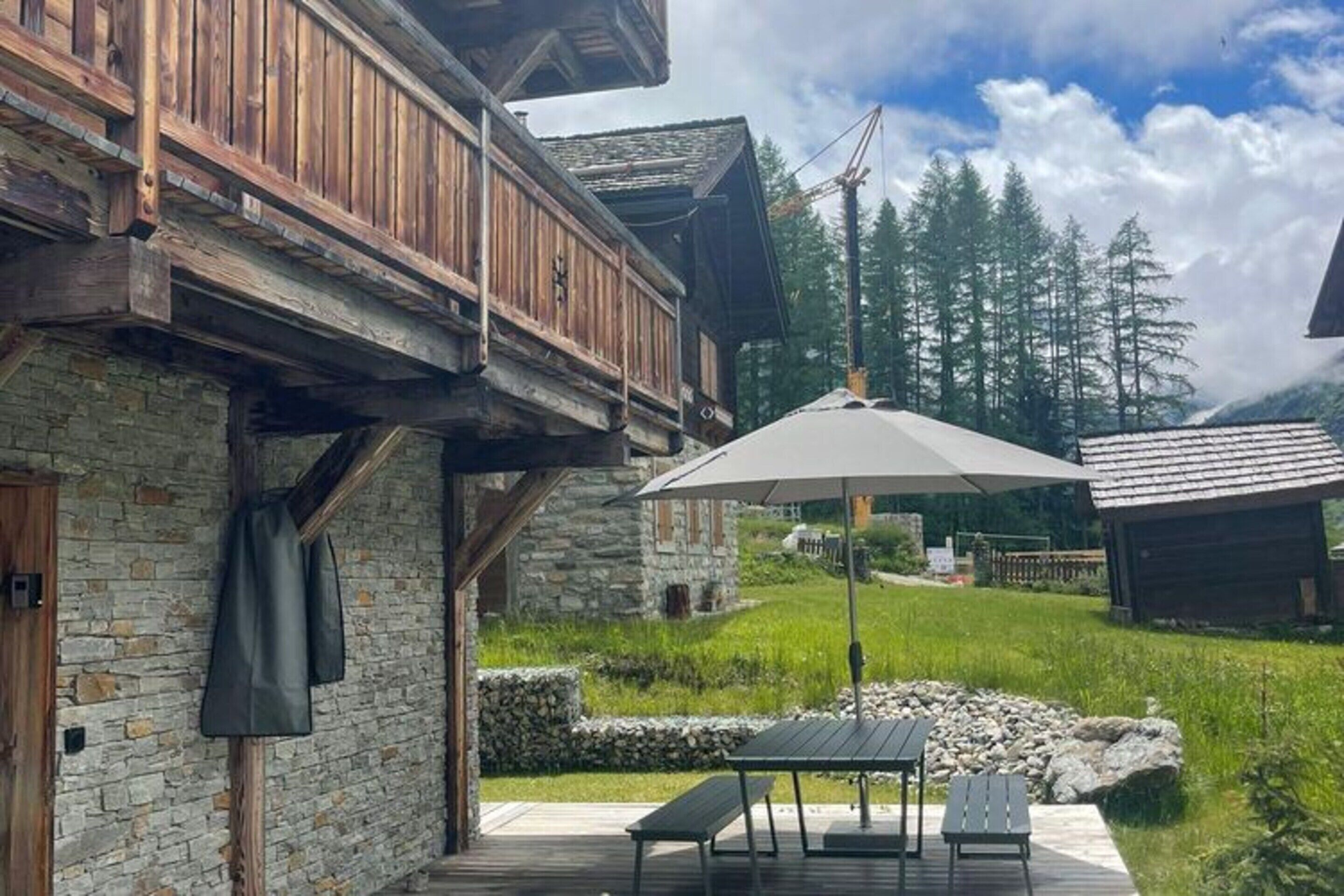 Un edificio rústico de madera con fachada de piedra, un balcón y un patio con mesa y sillas.