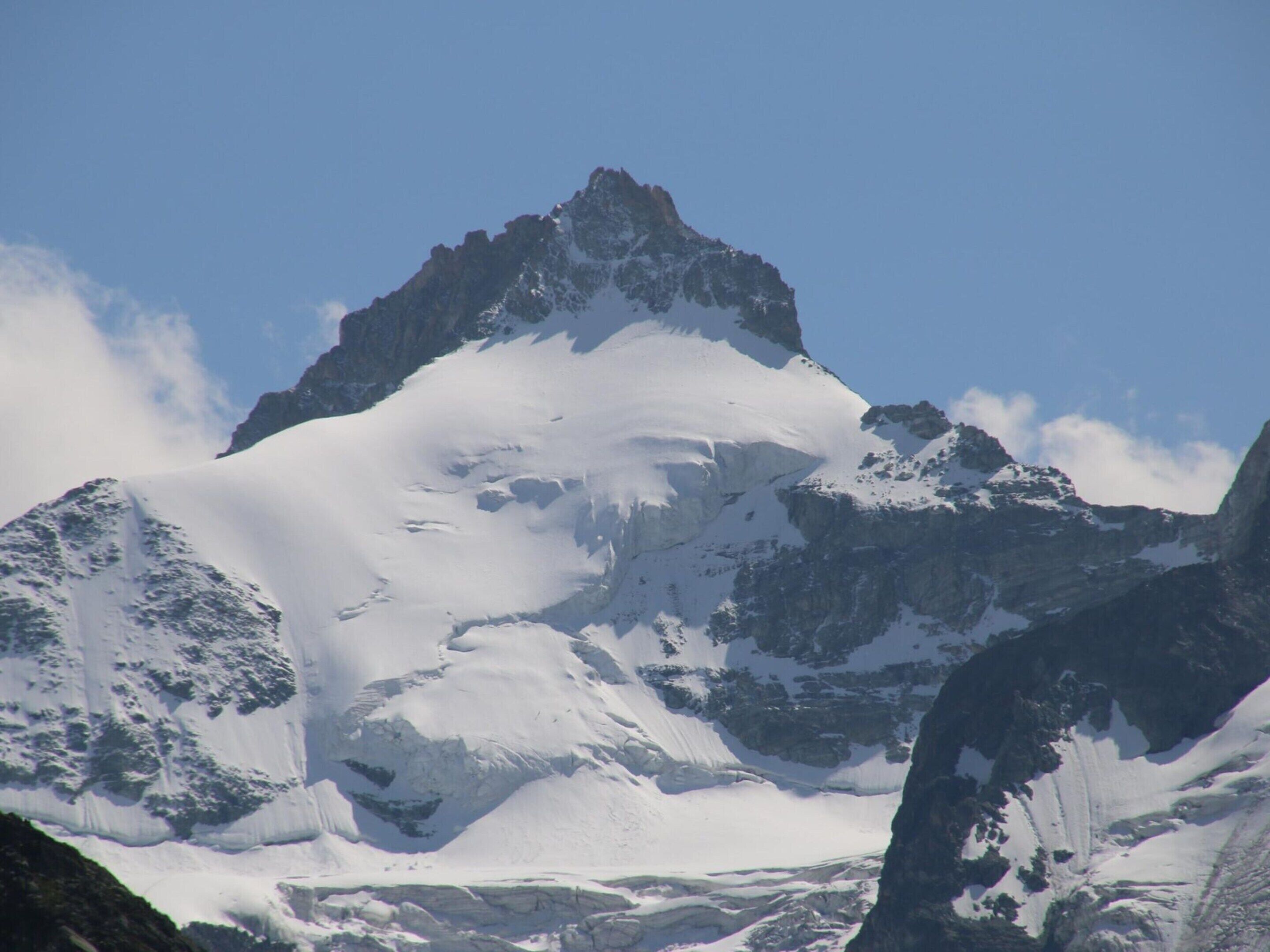 A snow-covered mountain peak with rugged terrain and a clear sky.