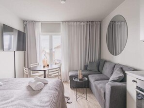 A modern hotel room with a bed, a sofa, a small table with a candle, a TV, and a view of the outside.
