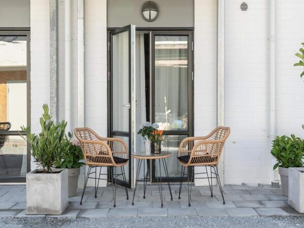 An outdoor seating area with two wicker chairs and a small table, flanked by potted plants.